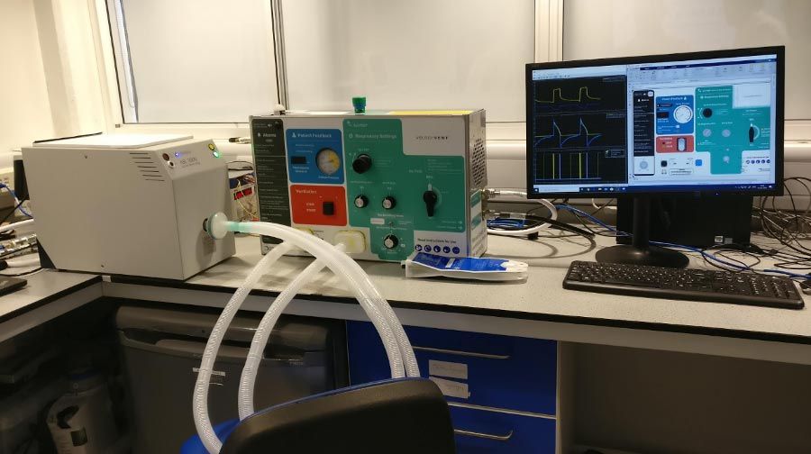 在办公室桌上,测试配置包括一个手语- 5000人工肺(左)和两个呼吸管连接到呼吸机(中间)。个人电脑右边是运行一个半实物的仿真软件模型测试。