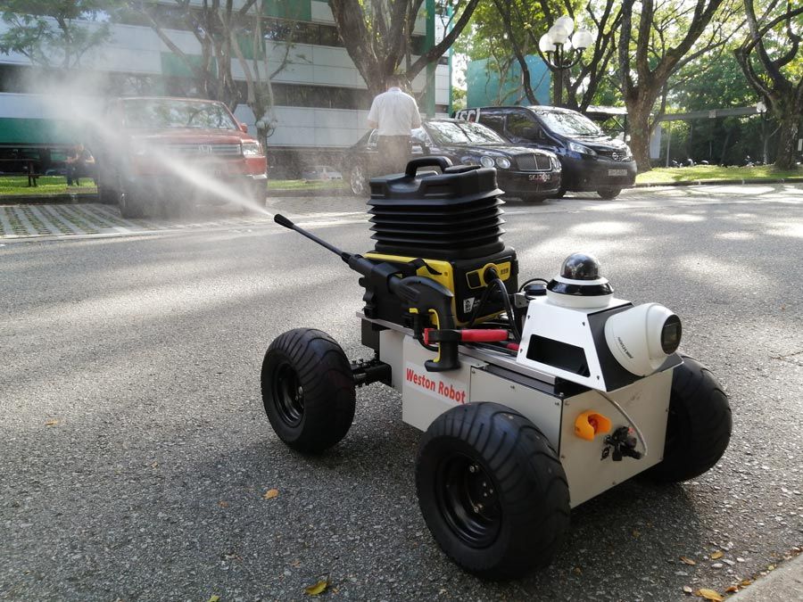韦斯顿机器人原型在铺好的街道上，积极地喷洒外面。图片的背景是汽车和一个人。